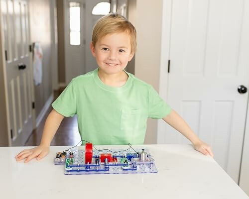 Young boy smiling with an electronic circuit kit on a table.